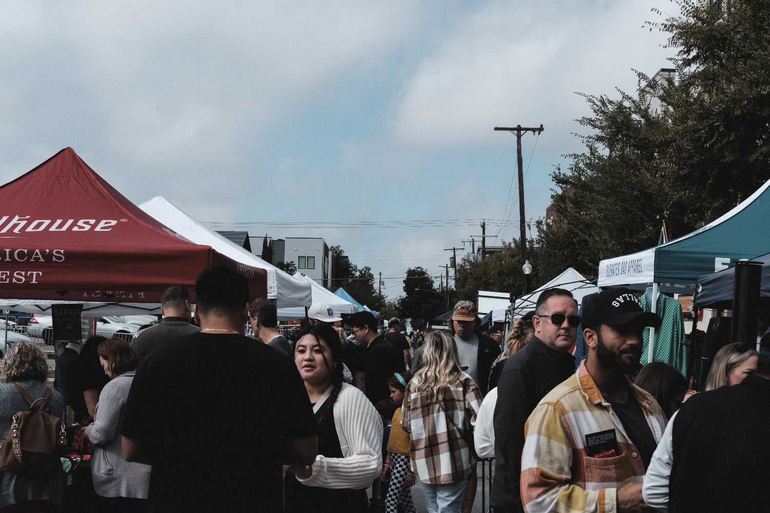 Crowd of people at an outdoor event with tents and a clear sky.